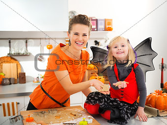 Smiling halloween dressed girl with young mother making biscuits