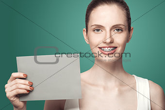 Beautiful girl with braces and gray card in hands