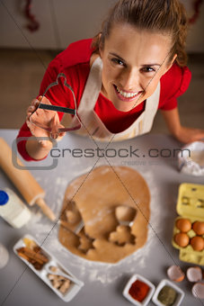 Young housewife showing Christmas cookie cutter while in kitchen
