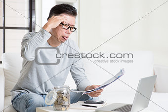 Stressed mature Asian man paying bill at home. 