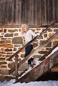 Cheerful woman in white sweater on stairs of cosy mountain house