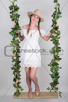 full-length Beautiful young leggy blonde in a little white dress and white cowboy hat on a swing, wooden swing suspended from a rope hemp, rope wrapped vine and ivy