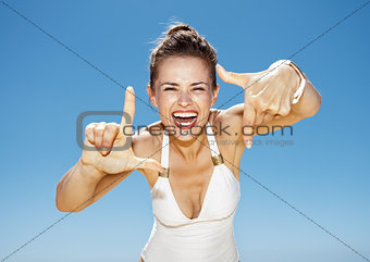 Smiling woman in swimsuit at sandy beach framing with hands