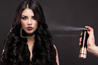 Beautiful brunette model: curls, classic makeup and red lips with a bottle of hair products. The beauty face.