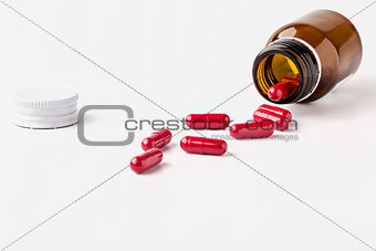 Open glass brown pill bottle and scattered red capsules