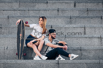 Young stylish couple on concrete stairs with a longboard