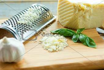 Heap of grated Parmesan on wooden background with leaf of basili