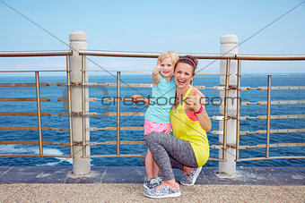 Happy fitness mother and child on embankment showing thumbs up