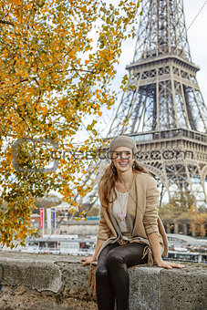 elegant woman sitting on parapet on embankment near Eiffel tower