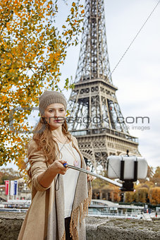 woman taking selfie using selfie stick on embankment in Paris