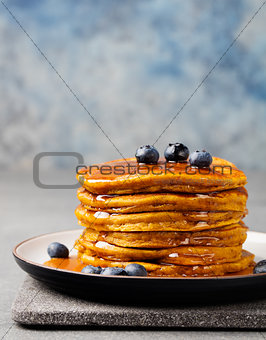 Pumpkin pancakes with maple syrup and blueberries on a plate. Grey stone background Copy space