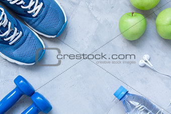 Flat lay sport shoes, dumbbells, earphones, apples, bottle of wa
