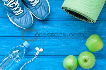 Flat lay sport shoes, bottle of water, mat and earphones on blue