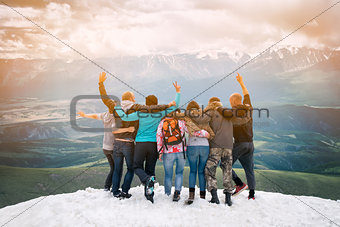 Group of friends are happy that climbed to the top  the mountain. They hug and jump. Looking into the distance with back  the camera.