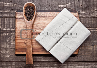 Pepper on spoon and kitchen towel on wooden board
