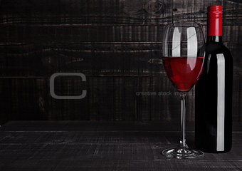 Bottle and glass of red wine on wooden background