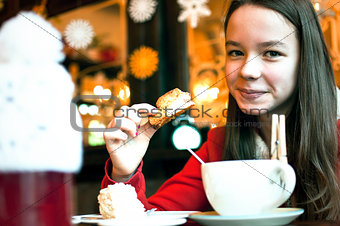Girl with a cup of tea in a cafe eating Christmas cookies and sm