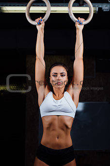 Portrait of young fit muscular girl in white top using gymnastic rings.