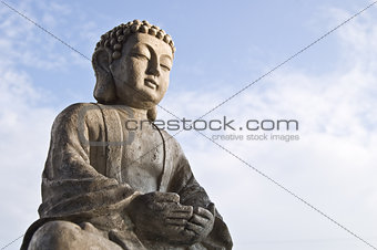 Sitting Buddha image in lotus position on sky background.