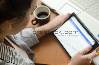 Young woman sitting at a laptop and holding a a tablet in hands
