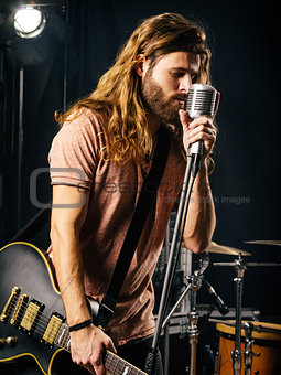 Young man singing and playing electric guitar on stage