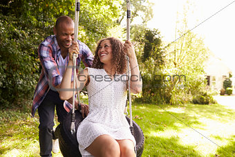 Man Pushing Woman On Tire Swing In Garden