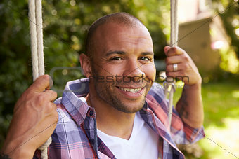 Head And Shoulders Shot Of Mid Adult Man Sitting On Swing