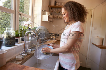 Woman Standing At Kitchen Sink Washing Up