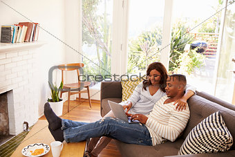 Couple Relaxing On Sofa At Home Using Laptop