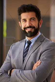 Smiling Hispanic businessman, arms crossed, close up vertical