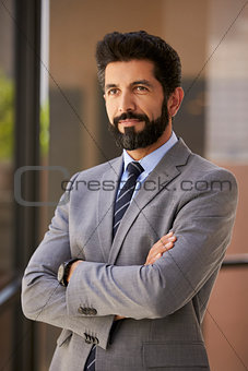 Hispanic businessman with arms crossed looks away, vertical