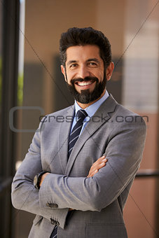 Smiling Hispanic businessman with arms crossed, vertical