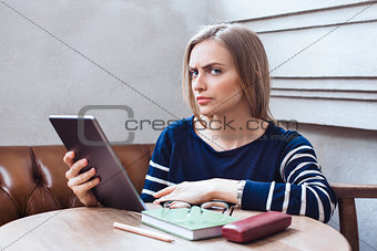 Beautiful girl with the tablet looks suspicious. Woman studying and relaxing being in a cafe.