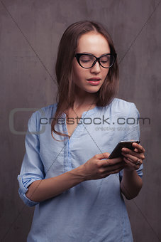 portrait of smiling woman with glasses and cellphone near grey background wall