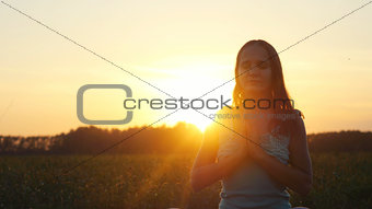 Young pretty brunette woman meditates in nature, in the field during beautiful sunset with lense flare effects