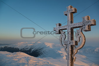 Frosted cross against beautiful sunrise scene in mountains
