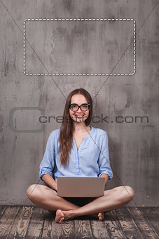 Young smiling woman sitting on the wooden floor with laptop