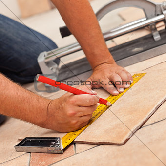 Laying ceramic floor tiles - man hands marking tile to be cut, c