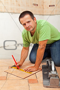 Man laying ceramic floor tiles - measuring and cutting one piece
