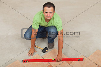Man laying ceramic floor tiles - checking with a level, top view