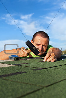 Man fastening bitumen roof shingles with nails and hammer