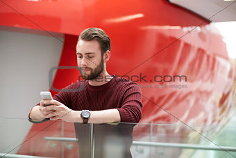 Bearded male student using smartphone in university building