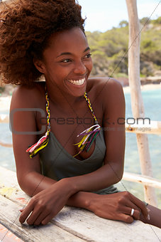 Black woman sitting at a table by the sea, vertical, Ibiza