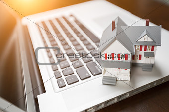 Miniature House And Laptop Computer Resting on Desktop.