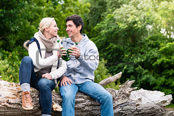 Lovers in vacation sitting at waterside clinking beer bottles