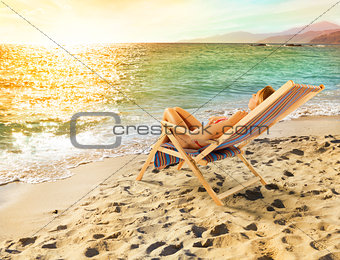 Girl tans on a deck chair on a beautiful beach