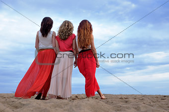 Young women in a long dress standing on the beach in summer evening.