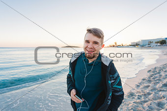 handsome portrait man listening to music smartphone, happy face, beard, beach, sea, travel, internet, Outdoor portrait, hipster style, holding phone in hand. beard man