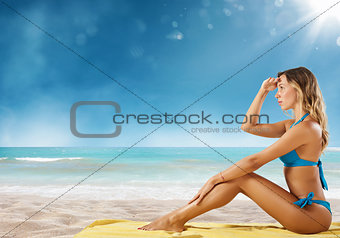 Girl in bikini sits on a beach looking for new travel destination.