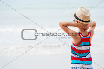 Boy in a hat and sunglasses admiring the sea